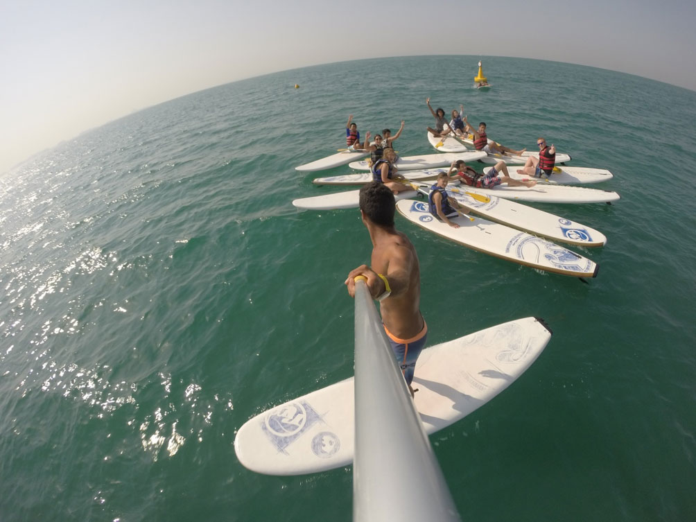 KIDS CAMP AND EXTRACURRICULAR ACTIVITIES: Group of children paddleboarding in the ocean during a kids camp, capturing the excitement of water sports and outdoor activities