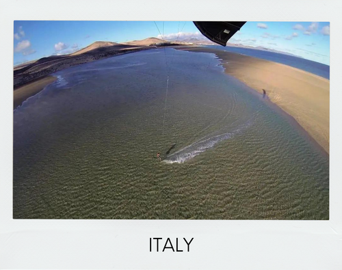 Kitesurfing in Italy: Aerial view of kitesurfing spot in Sardinia with kitesurfer on the water.